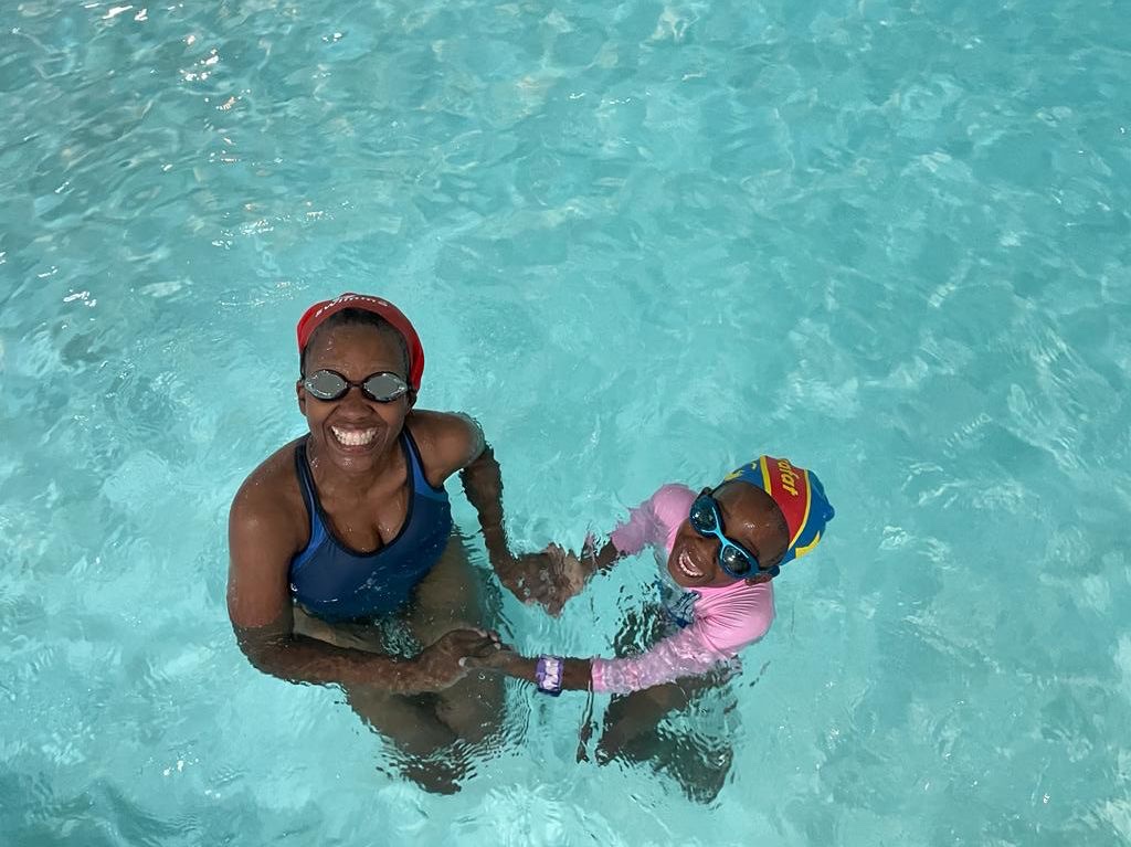 Sharon smiling with a young student in a swimming pool during a kids' learn-to-swim lesson.
