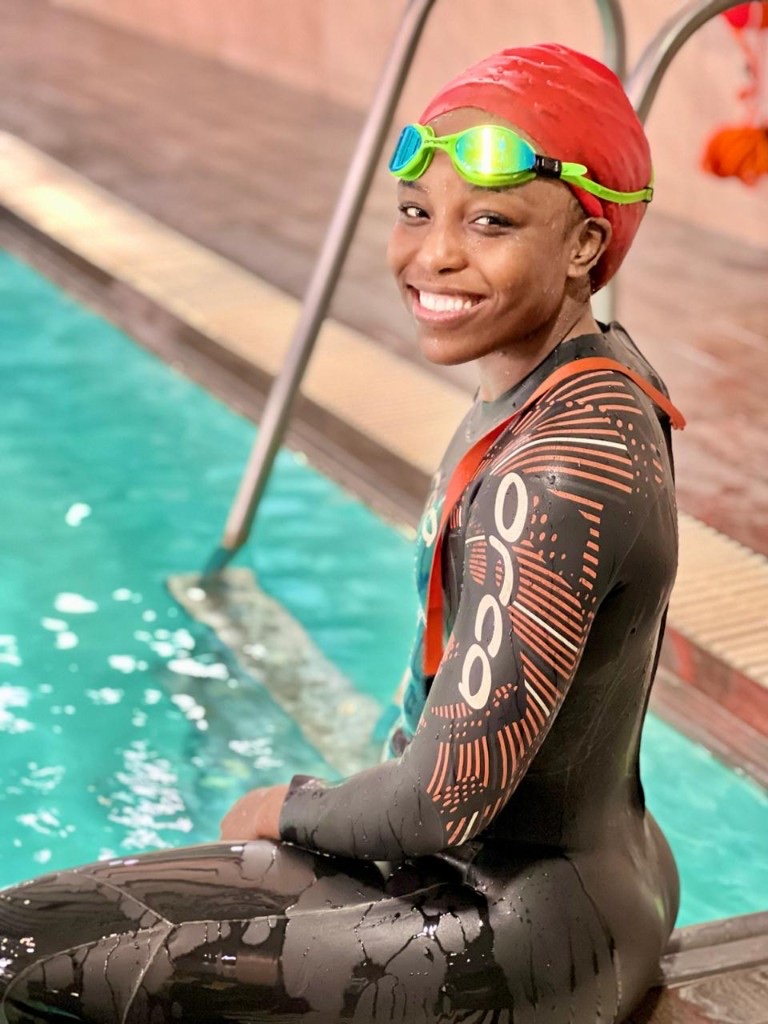 Sharon in a wetsuit by the pool, smiling at the camera